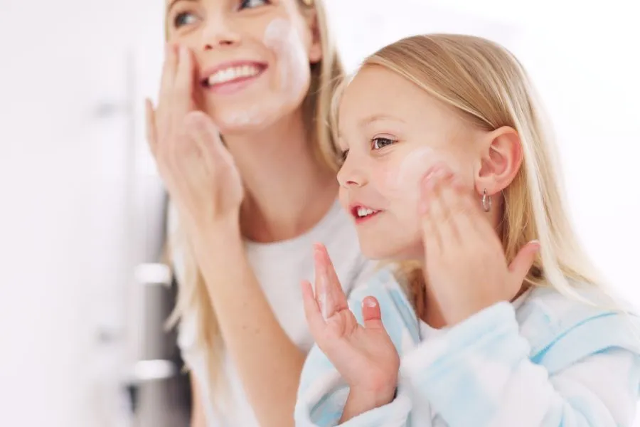 A mother and daughter both putting cream on their face.